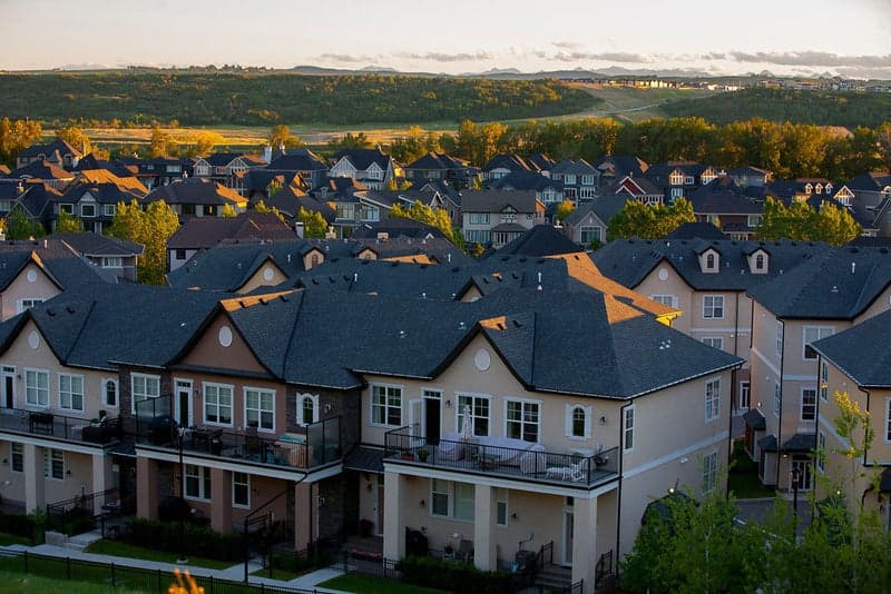 Rooftops across a Calgary neighbourhood at sunrise, with the foothills behind